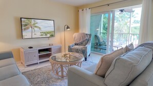 A living room with a sofa, a glass coffee table, a chair, a TV, and a balcony with outdoor furniture. - Tropical Getaway (Sanibel)
