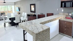 Eine moderne Küche mit Granit-Arbeitsplatten, weißen Schränken und einem Essbereich mit weißen Stühlen.
