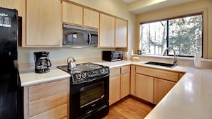 A modern kitchen with wooden cabinets, a stainless steel stove, a microwave, and a large window offering a view of trees.