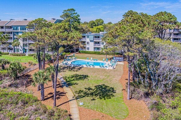 A pool area with lounge chairs, surrounded by trees and buildings.