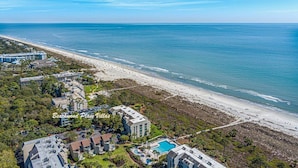 Ett flygbildsfoto av ett hotell vid kusten med utsikt över stranden, bestående av flera byggnader och med en swimmingpool.