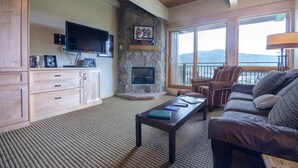 Una sala de estar con chimenea de piedra, televisor de pantalla plana, sofá y balcón con vistas.