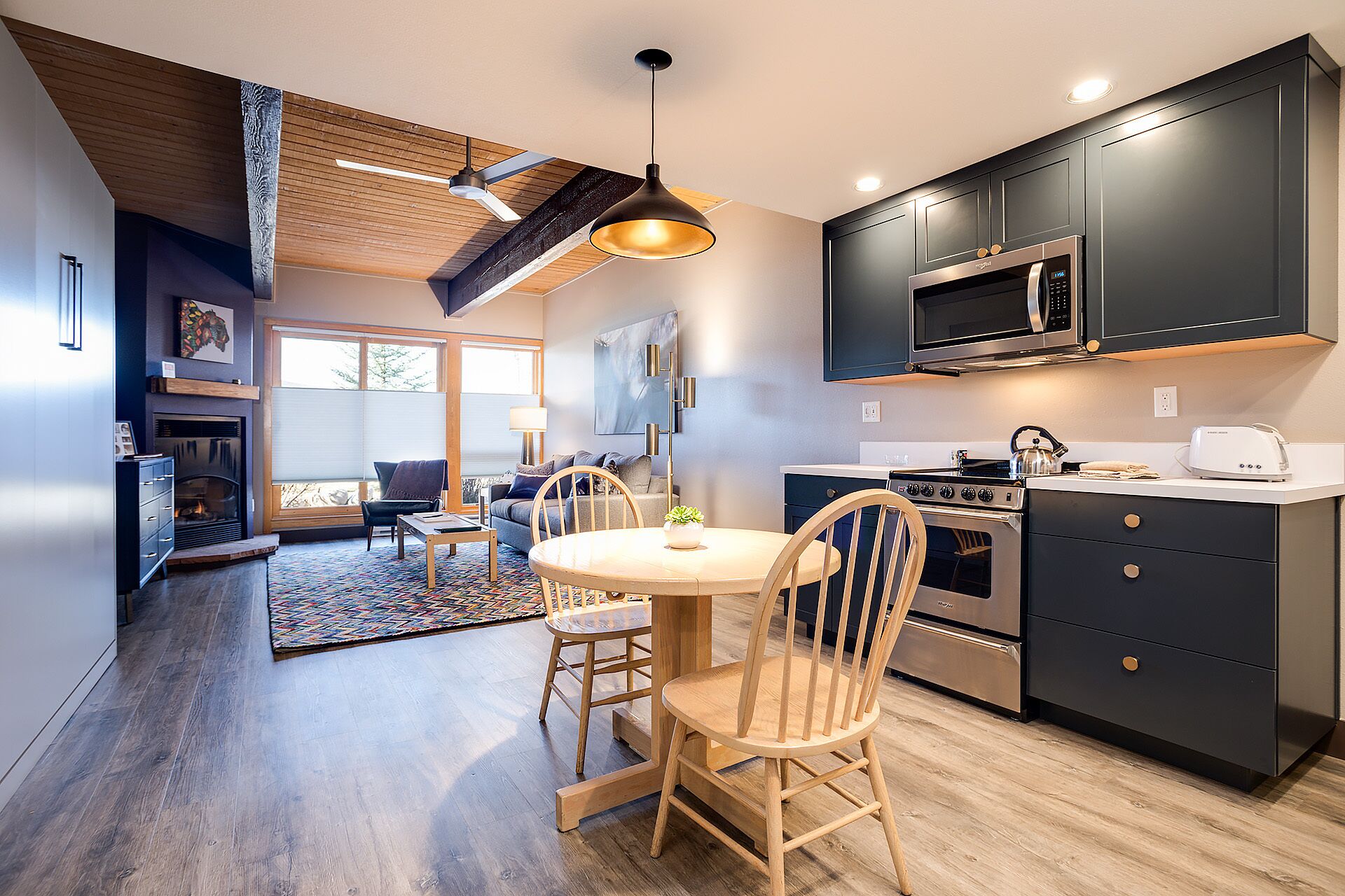 Une cuisine moderne avec des meubles de couleur sombre, un four à micro-ondes encastré et une cuisinière. On y trouve également un coin repas avec une table ronde et des chaises en bois.