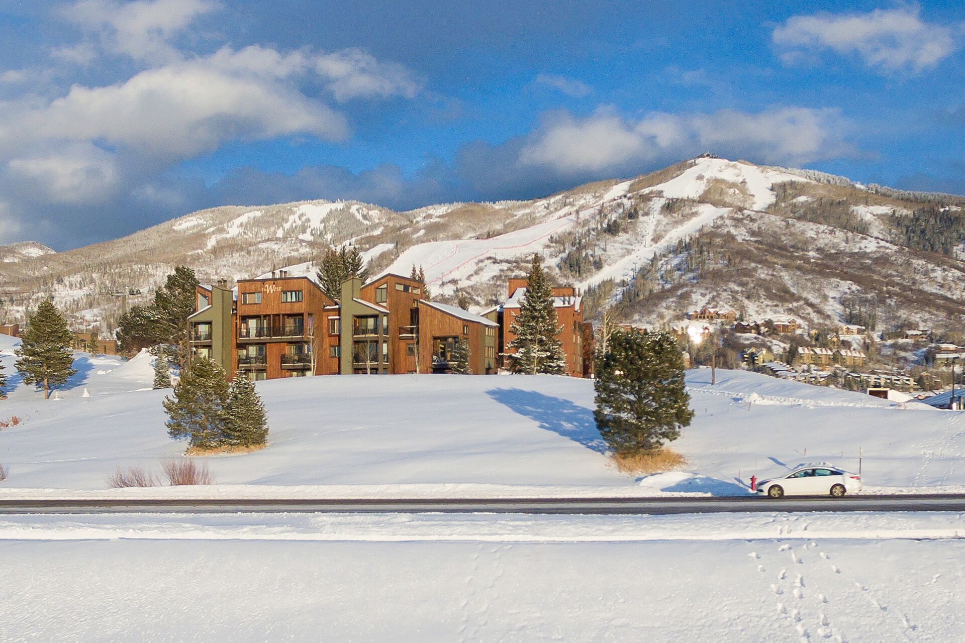 Un hotel moderno con fachada de madera, ubicado en una ladera nevada con montañas al fondo.