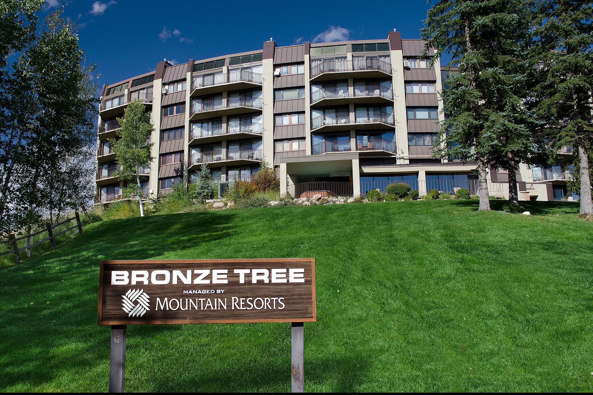 Un edificio de varios pisos con balcones, un primer plano con césped y un letrero que indica que es administrado por Mountain Resorts.