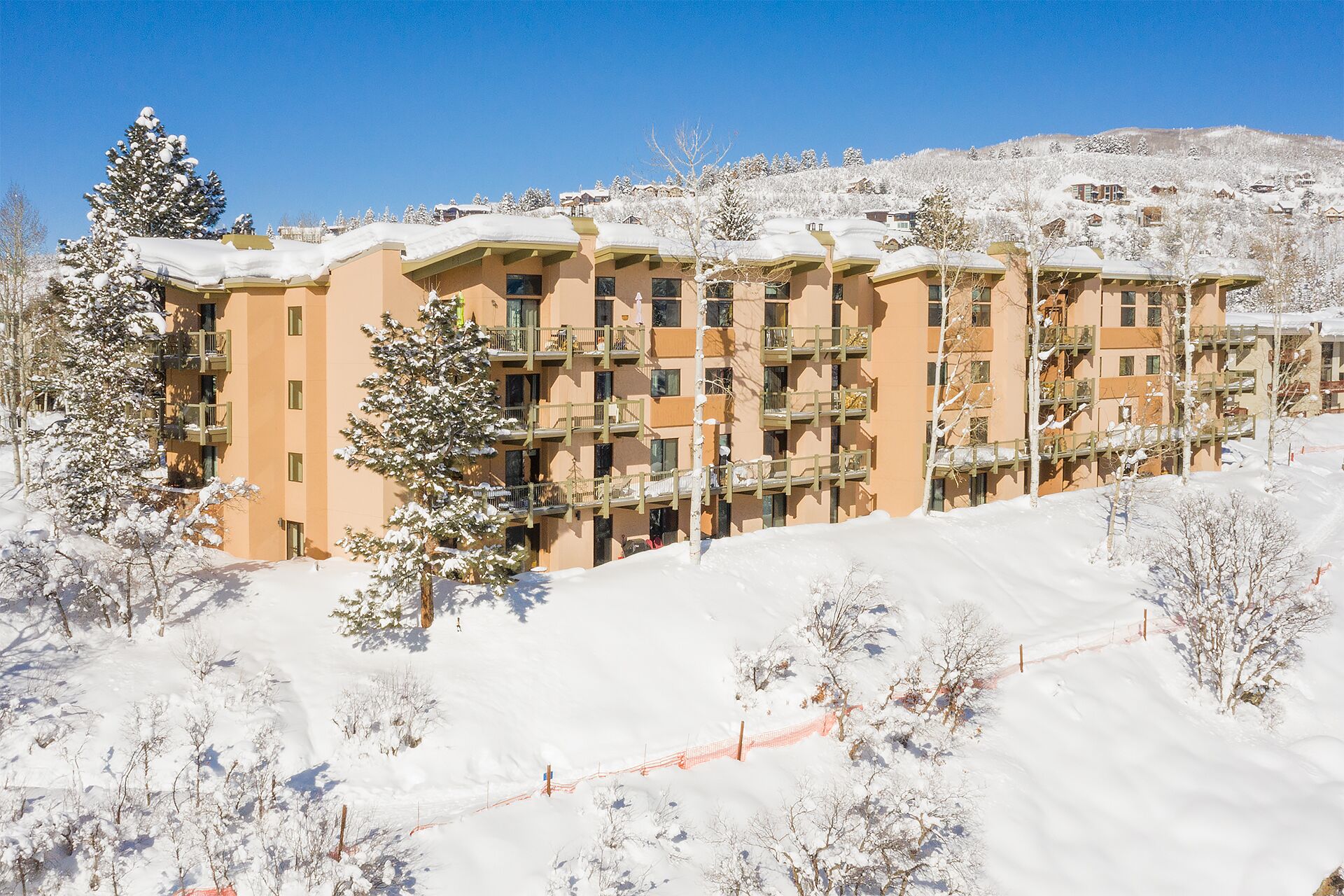 Un hotel a più piani con balconi, circondato da alberi innevati e una pista da sci.