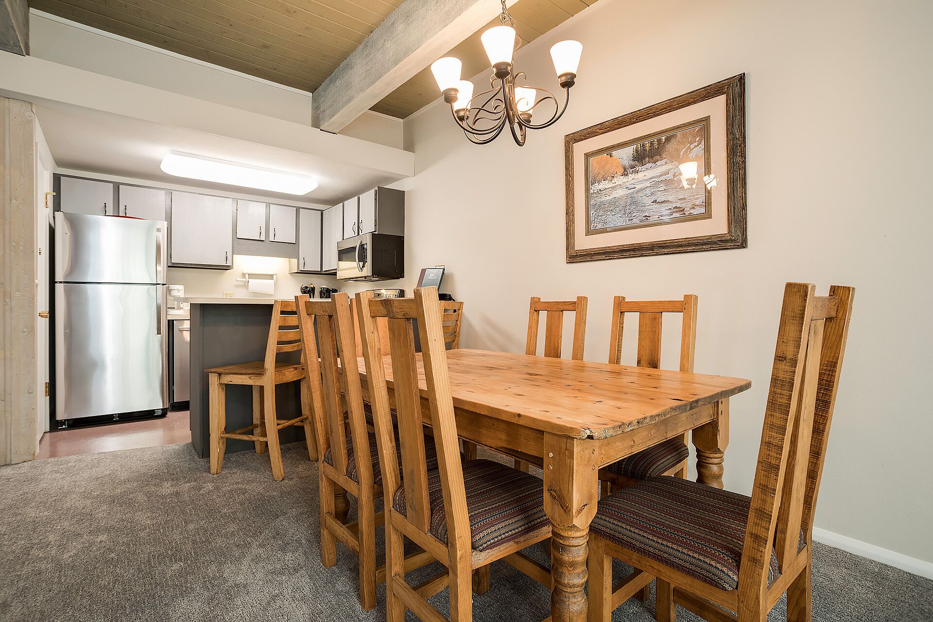 A dining area with a wooden table and chairs, a chandelier, and a framed picture on the wall.