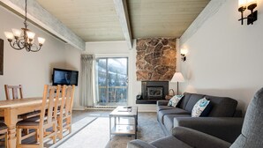 Una sala de estar acogedora con chimenea de piedra, un sofá, una mesa de comedor con sillas y un televisor.