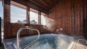 Ein Whirlpool mit Metallleiter, aufsteigender Dampf, Holzwände und Blick auf Gebäude im Freien.