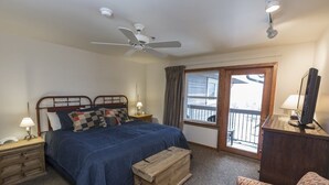 Une chambre à coucher comprenant un lit, une commode en bois, une table de chevet avec une lampe, une coiffeuse, un ventilateur de plafond et une fenêtre donnant sur un beau paysage.
