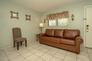 A room with a brown leather sofa, a matching armchair, and a small table with a lamp.