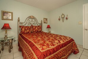 A bedroom with a bed, two bedside tables, a nightstand, a wall clock, and a door.