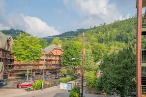 A multi-story building with a parking lot in front, surrounded by lush greenery and a hilly landscape.
