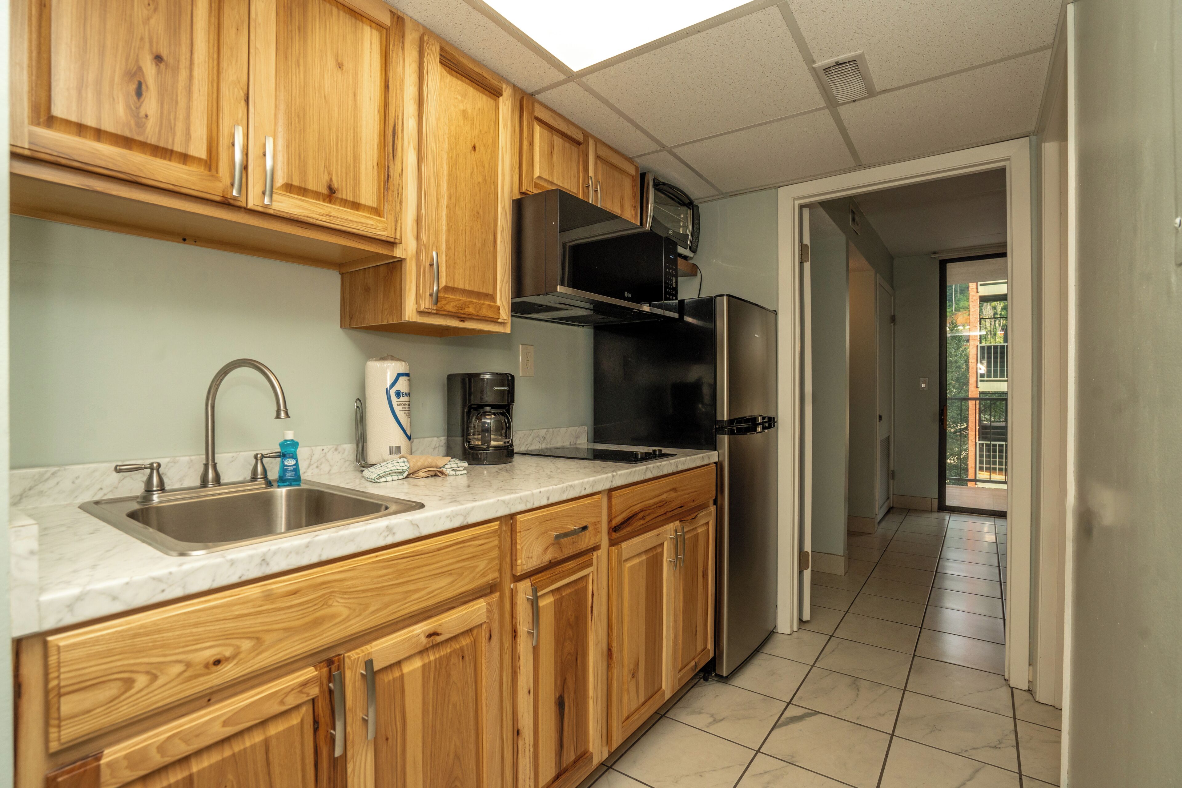 A kitchen with wooden cabinets, a stainless steel sink, a coffee maker, and a refrigerator.