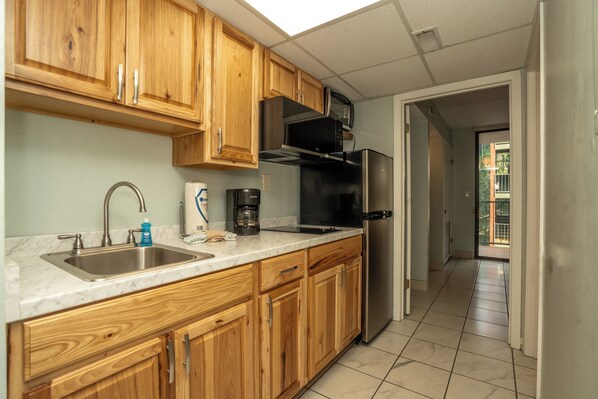 A kitchen with wooden cabinets, a stainless steel sink, a coffee maker, and a refrigerator.