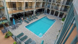 Un edificio de varios niveles con un patio central que cuenta con piscina, sillones de descanso y sombrillas.