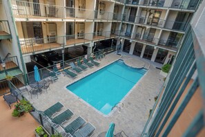 A multi-level building with a central courtyard featuring a swimming pool, lounge chairs, and umbrellas.
