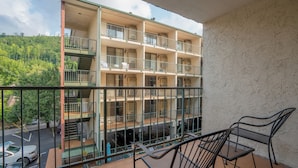 Un edificio de varios pisos con balcones, mobiliario exterior y vistas a un estacionamiento.