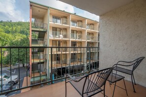 A multi-story building with balconies, outdoor seating, and a view of a parking area.