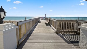 A wooden boardwalk leading to the beach with a lamp post on the left.