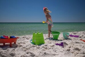 A beach scene with a child playing with sand toys, a green sandcastle, and a red play structure. - El Matador 410 by Alicia Hollis Rentals FREE TICKETS! $300/Day (Fort Walton Beach)