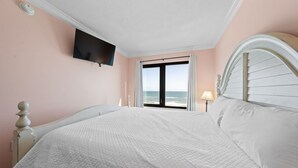 Una camera da letto con un letto grande, una TV montata a parete, una finestra vista mare e una lampada sul comodino.