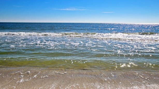 Una spiaggia con acque cristalline e onde, una riva sabbiosa e un cielo azzurro limpido.