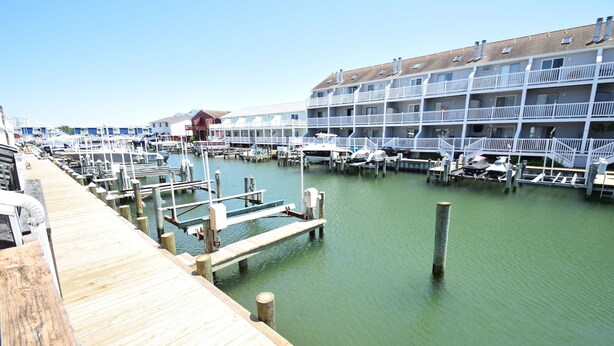 A marina with docked boats, a wooden pier, and a multi-story building with balconies. - Crab Harbour 4-Baywater 28th St, W/D, AC (Ocean City)
