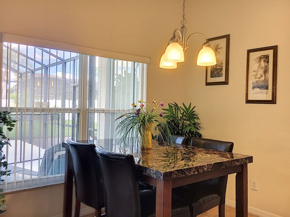 Un coin repas avec une table en marbre, des chaises noires, une plante en pot et un luminaire suspendu.