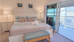 A bedroom with a bed, two nightstands, a bench, and a view of the balcony. - Enjoy Island Living (Sanibel)