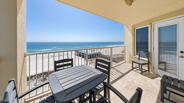 Un balcon avec une table et des chaises, une vue sur la plage et une porte avec une fenêtre.