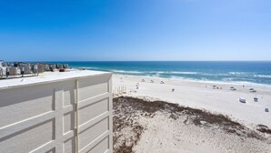 Vue sur la plage depuis un immeuble à la façade blanche et au toit plat.
