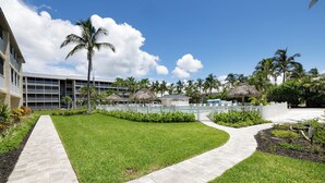 A well-maintained outdoor area with a paved walkway, palm trees, and a building with multiple floors and balconies. - Bright And Beachy (Sanibel)