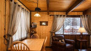 L’intérieur chaleureux d’un chalet avec une table à manger en bois, un canapé en cuir et une fenêtre agrémentée de rideaux.