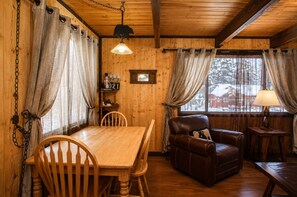 Interior acogedor de una cabaña con mesa de comedor de madera, sofá de cuero y una ventana con cortinas.