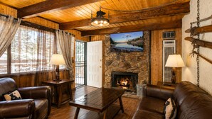 A cozy cabin interior with leather furniture, a stone fireplace, and a television mounted on the wall. - Bear 'n Tree - Walk to Lake & Village, Fireplace, Barbecue (Big Bear Lake)