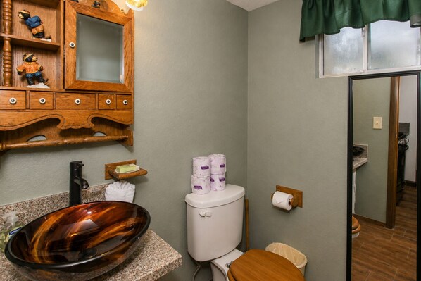 Une salle de bain avec un meuble-lavabo en bois, un lavabo sur colonne, des toilettes et un miroir.