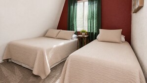 Two twin beds with beige bedding in a room with a red accent wall and a window with green curtains. - Bear 'n Tree - Walk to Lake & Village, Fireplace, Barbecue (Big Bear Lake)