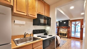 A kitchen with wooden cabinets, a stainless steel sink, a black microwave, a stove, and a stone fireplace. - Managed by Park City Lodging-One Block to Park City Mtn's Quit'N Time Ski Run (PARK CITY)