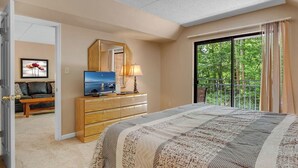 A bedroom with a large bed, a dresser, a TV, and a balcony with a view of trees. - two bedroom condo sleeps 4 persons (Gatlinburg)