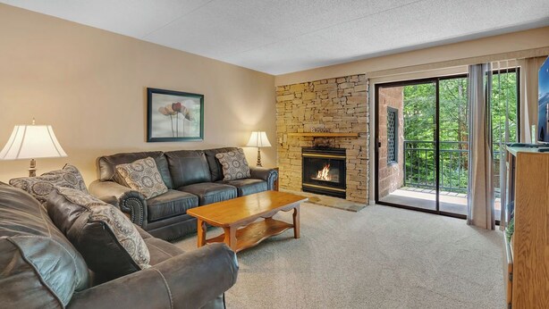 A living room with a stone fireplace, leather sofas, and a view through a glass door to the outdoors. - two bedroom condo sleeps 4 persons (Gatlinburg)