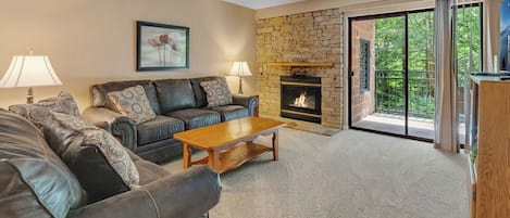 Una sala de estar con chimenea de piedra, sofás de cuero y vistas al exterior a través de un ventanal.