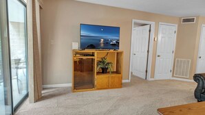 A living room with a flat-screen TV on a wooden stand, a potted plant, and a sliding glass door leading to a balcony. - two bedroom condo sleeps 4 persons (Gatlinburg)