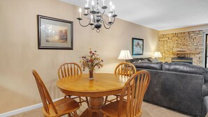 A dining area with a wooden table and chairs, a chandelier, and a stone wall in the background. - two bedroom condo sleeps 4 persons (Gatlinburg)
