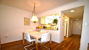 En matplats med ett vitt bord och stolar, en hängande lampa och ett kök i bakgrunden.