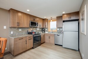 Your fully equipped kitchen features warm wood cabinetry, granite countertops, and modern stainless appliances—perfect for preparing meals while enjoying natural light and mountain vistas through the window.