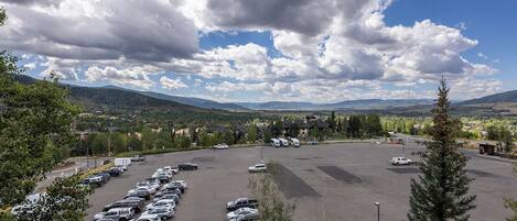 A parking lot with multiple cars and a view of a residential area with houses and mountains in the background.