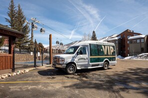 Un autobús lanzadera VIP blanco y verde estacionado en un estacionamiento, con un telesilla al fondo.