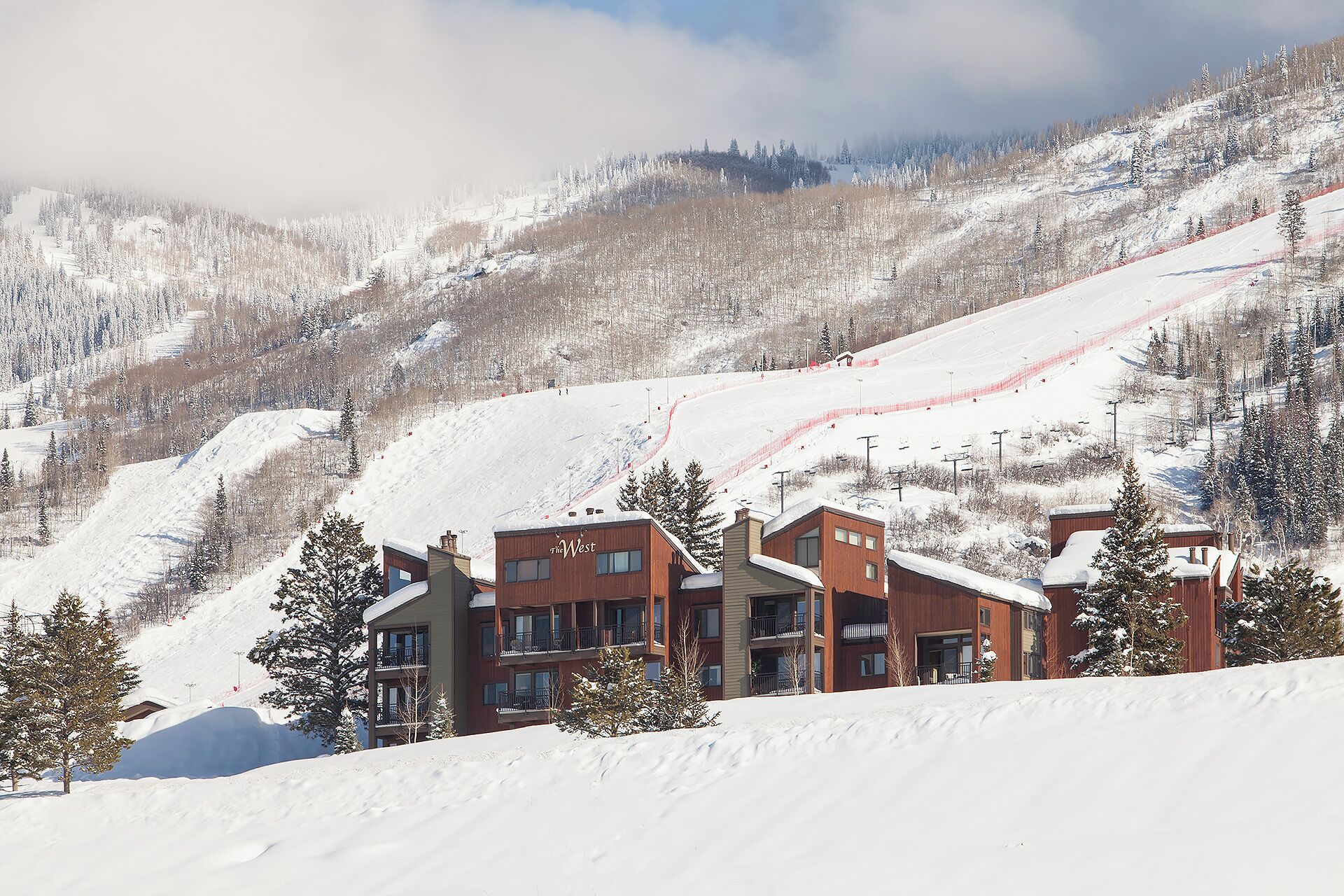 Une montagne enneigée, avec une piste de ski et un ensemble de bâtiments comprenant plusieurs étages et des balcons.