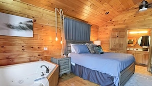 Une chambre dans une cabane en bois, avec un grand lit, une table de chevet en bois, une baignoire et un miroir.